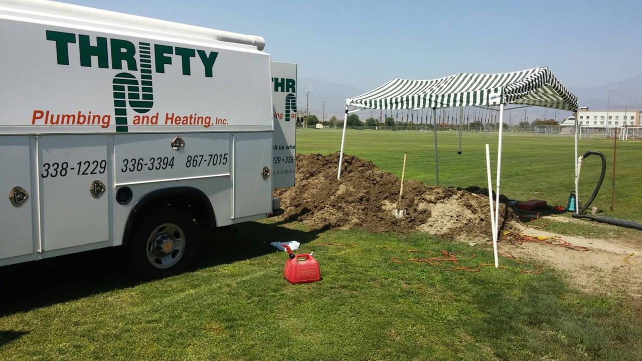 Thrifty Plumbing and Heating truck parked at an underground pipe repair, with the excavation, shovel and work canopy beside it