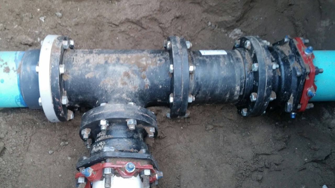 New ductile-iron tee with flanged and restrained fittings joining PVC water main pipe in an excavation